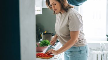 Kvinde står i køkkenet og laver mad.