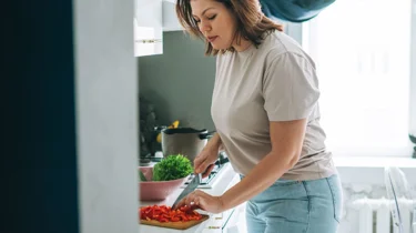 Kvinde står i køkkenet og laver mad.