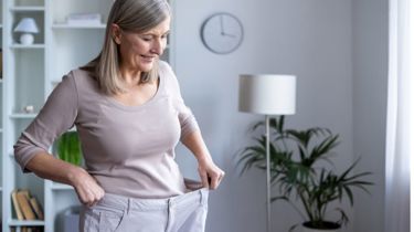 Glad ældre kvinde iført sine for store bukser, som passede inden hun fik lavet fedmeoperation ved Aleris.