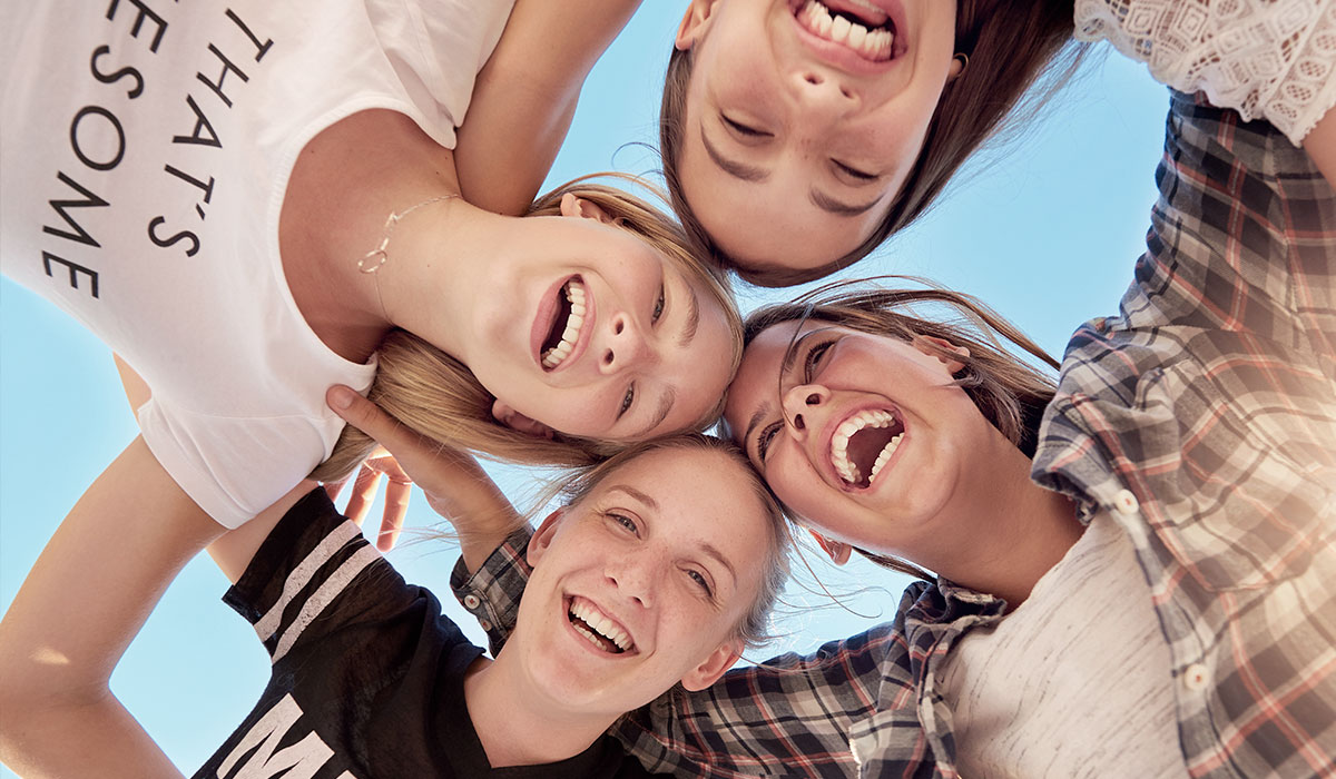 Et billede af gode veninder, der længer sig ind over kameraet og smiler og griner