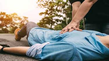 En person giver hjertelungeredning til en person som ligger på en vej.