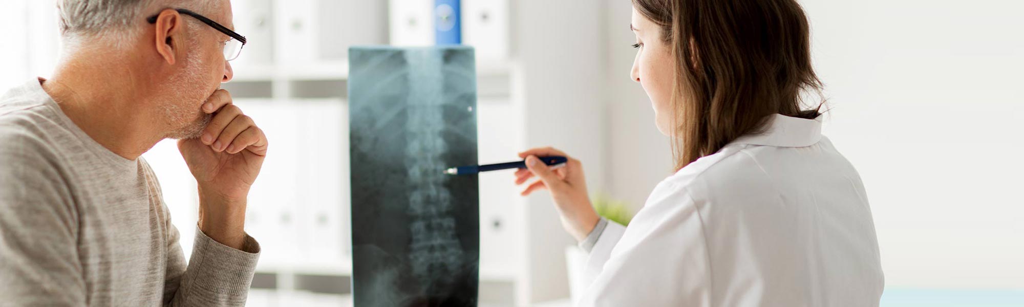 Læge og patient sidder og kigger på patientens røntgenbillede af hans rygsøjle.