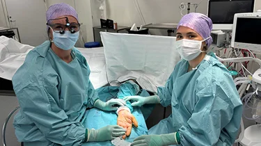 To kirurger med fuldt operationsudstyr kigger ind i kameraet.