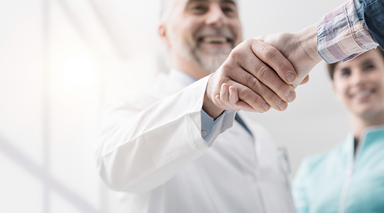 Læge giver smilende hånd til en patient.