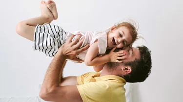 Far løfter sin grinende datter op i luften.