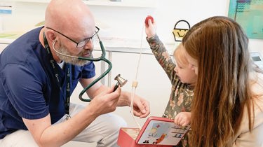 Børnelæge taler med mor og barn i konsultation omkring mavesmerter.