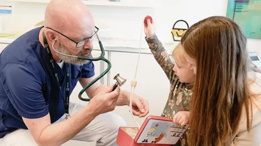 Børnelæge taler med mor og barn i konsultation omkring mavesmerter.