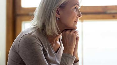 Trist, midaldrende kvinde sidder med hænderne under hagen og kigger ud af vinduet.