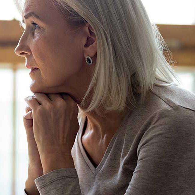 Kvinde sidder eftertænksomt og kigger ud i luften.