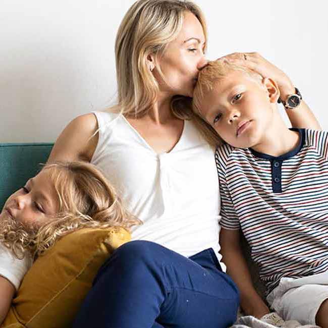 Mor sidder med sine to børn i sofaen.