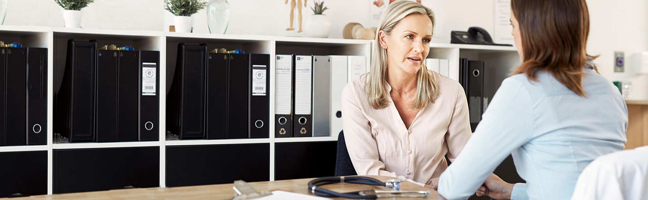 Kvinde sidder ved lægen og snakker om muskelknuder i underlivet.