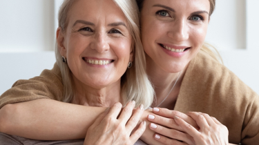 Et portræt af en mor og voksen datter, som holder om hinanden og smiler til kameraet