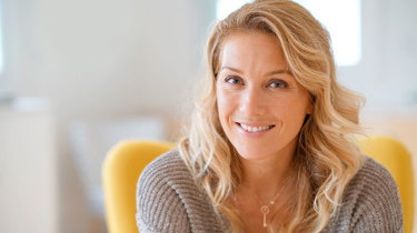 Kvinde 40+ sidder i en gul stol og smiler in i kameraet.