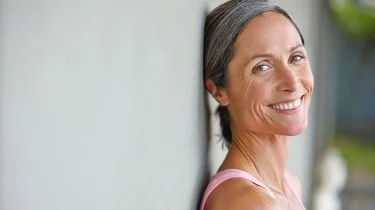 Midaldrende kvinde læner sig op ad en væg og smiler ind i kameraet.