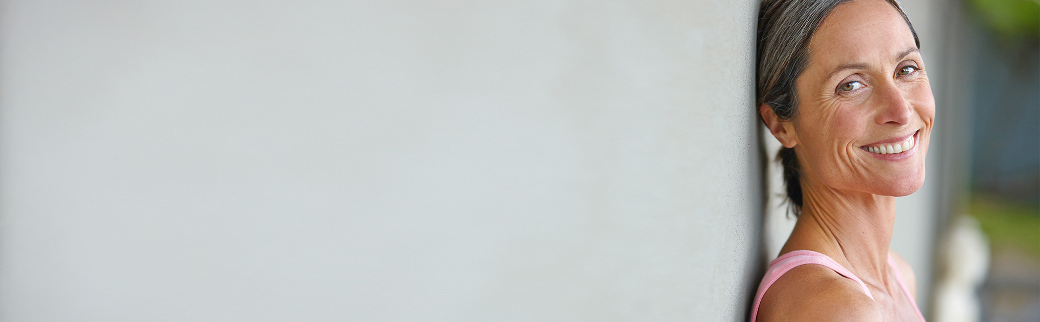 Midaldrende kvinde læner sig op ad en væg og smiler ind i kameraet.