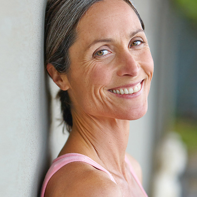 Midaldrende kvinde læner sig op ad en væg og smiler ind i kameraet.