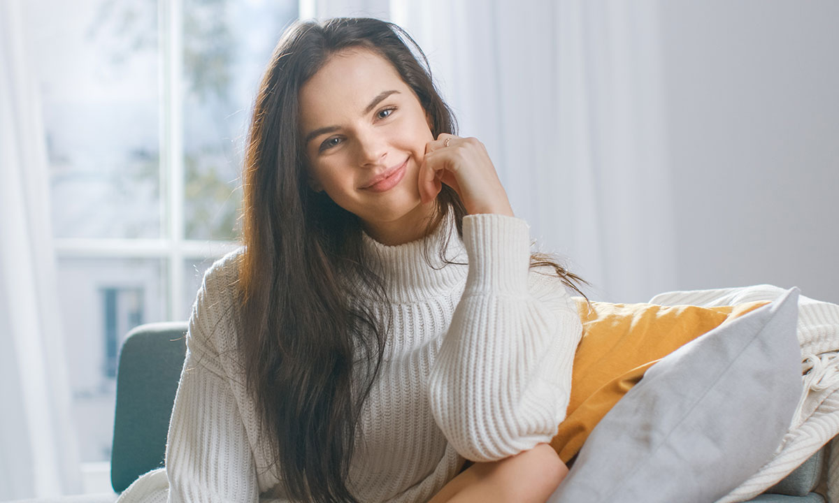 Glad kvinde sidder i sofa og smiler.