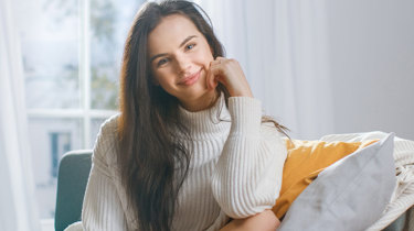 Glad kvinde sidder i sofa og smiler.