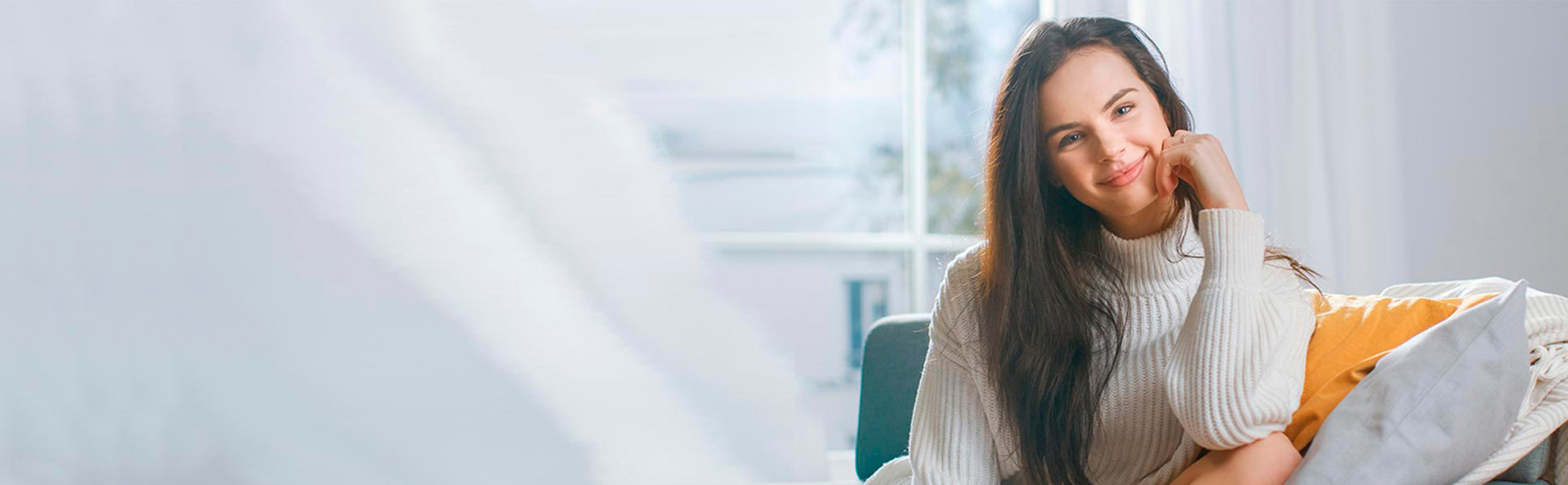 Glad kvinde sidder i sofa og smiler.