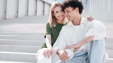 Et ungt par holder on hinanden på en trappe - hun smiler ind i kameraet mens han ser ned.