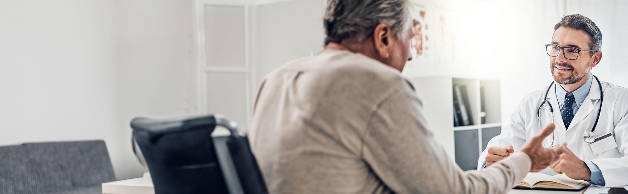 Mand sidder hos lægen og får forklaret mulige helbredsundersøgelser hos Aleris.