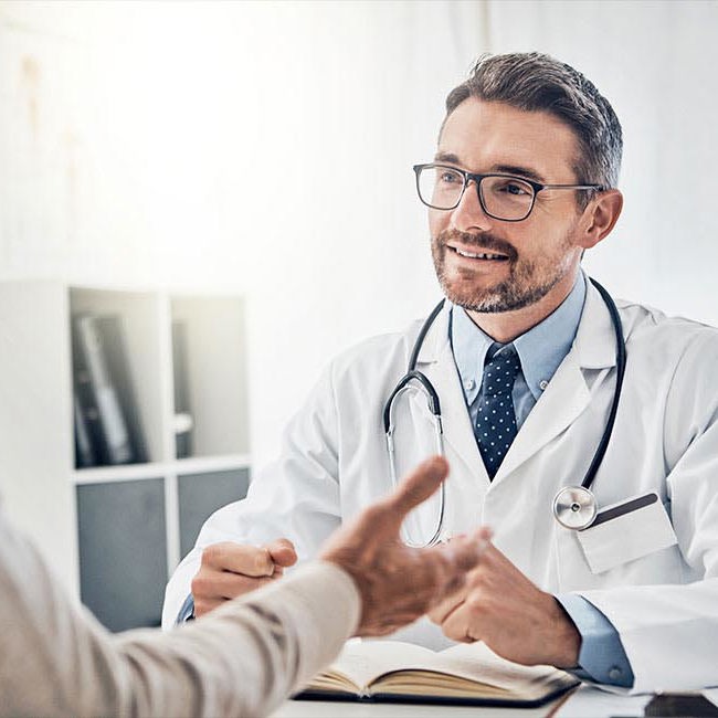 Mand sidder hos lægen og får forklaret mulige helbredsundersøgelser hos Aleris.