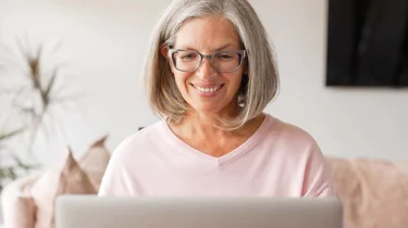 Kvinde sidder smilende ved sin computer.