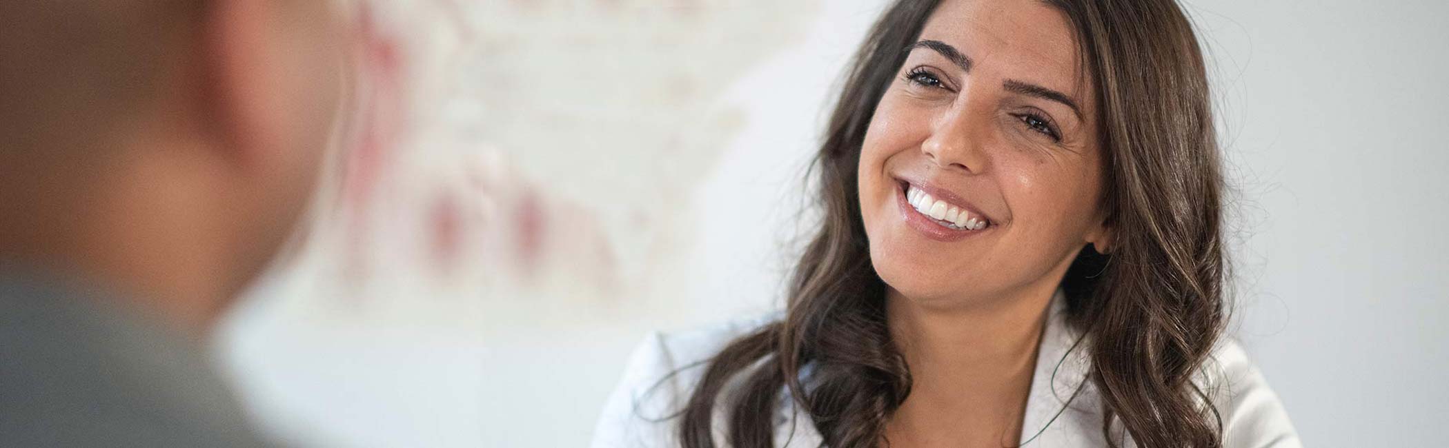 En kvindelig behandler sidder smilende og kigger på en patient.