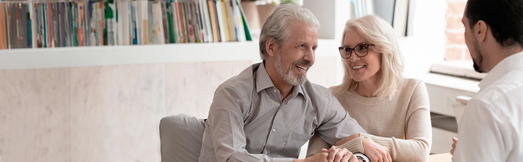 En mandlig audiolog sidder overfor et smilende ældre par, der får rådgivning om høreapparater