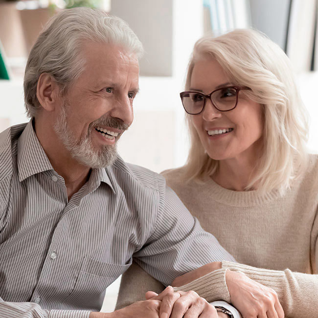 En mandlig audiolog sidder overfor et smilende ældre par, der får rådgivning om høreapparater