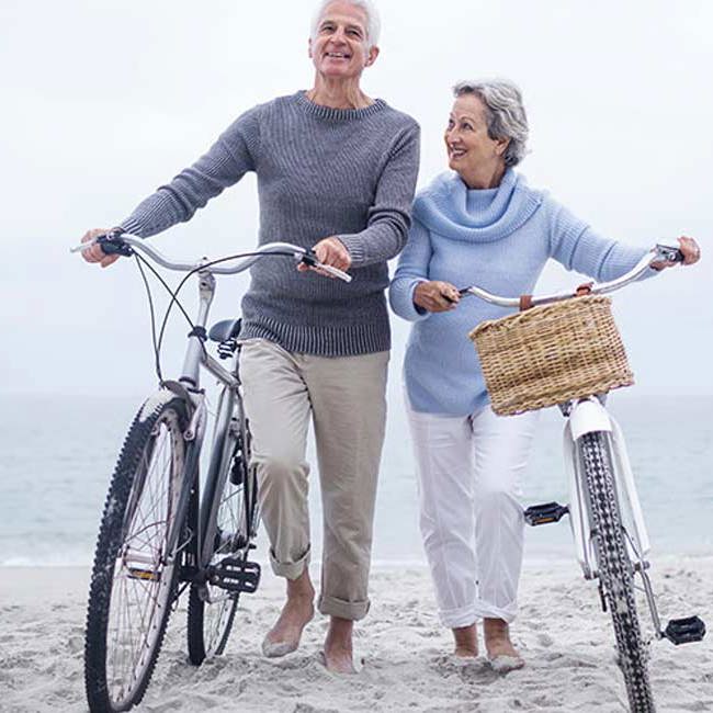 Ægtepar går med deres cykler på stranden.