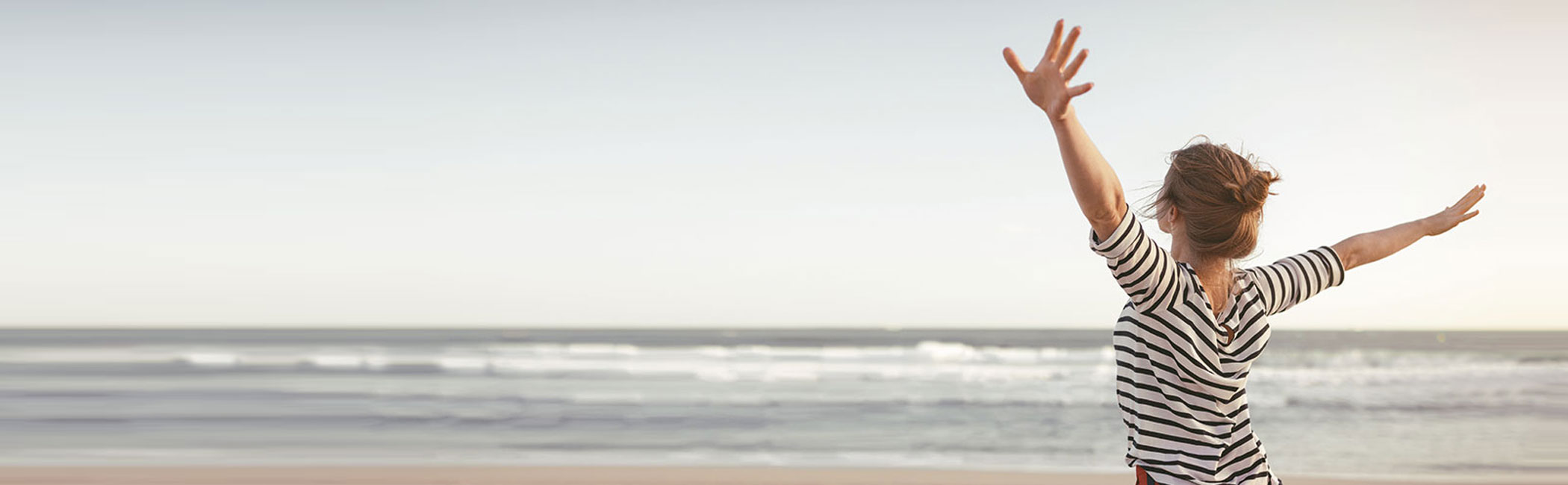 Kvinde strækker sig med armene i vejret på stranden.