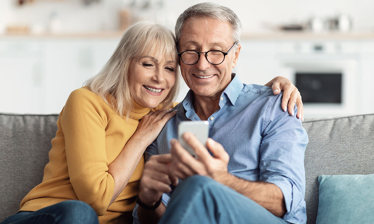 Et par sidder smilende og kigger på telefonen.
