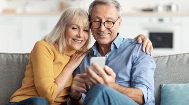 Et par sidder smilende og kigger på telefonen.