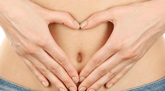 Kvinde laver et hjerte med sine hænder og holder det rundt om sin nygravide mave.