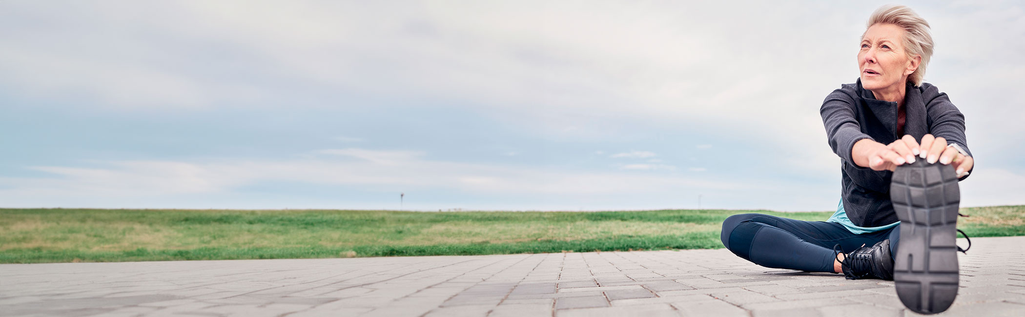 Kvinde sidder på jorden og strækker ud efter en løbetur.