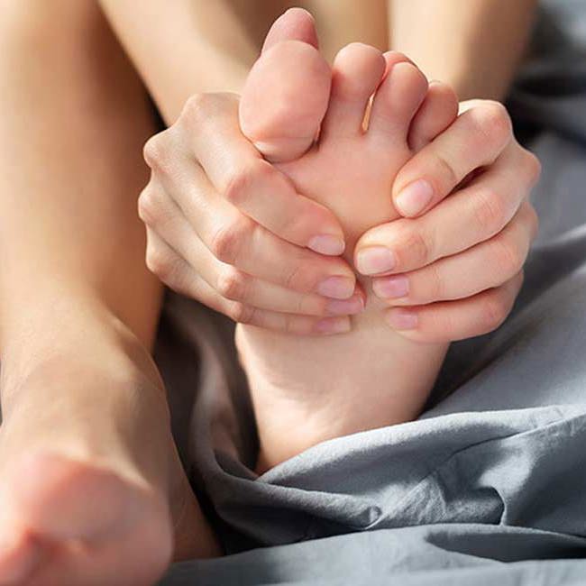 En kvinde masserer sine fødder ved fodsmerter.