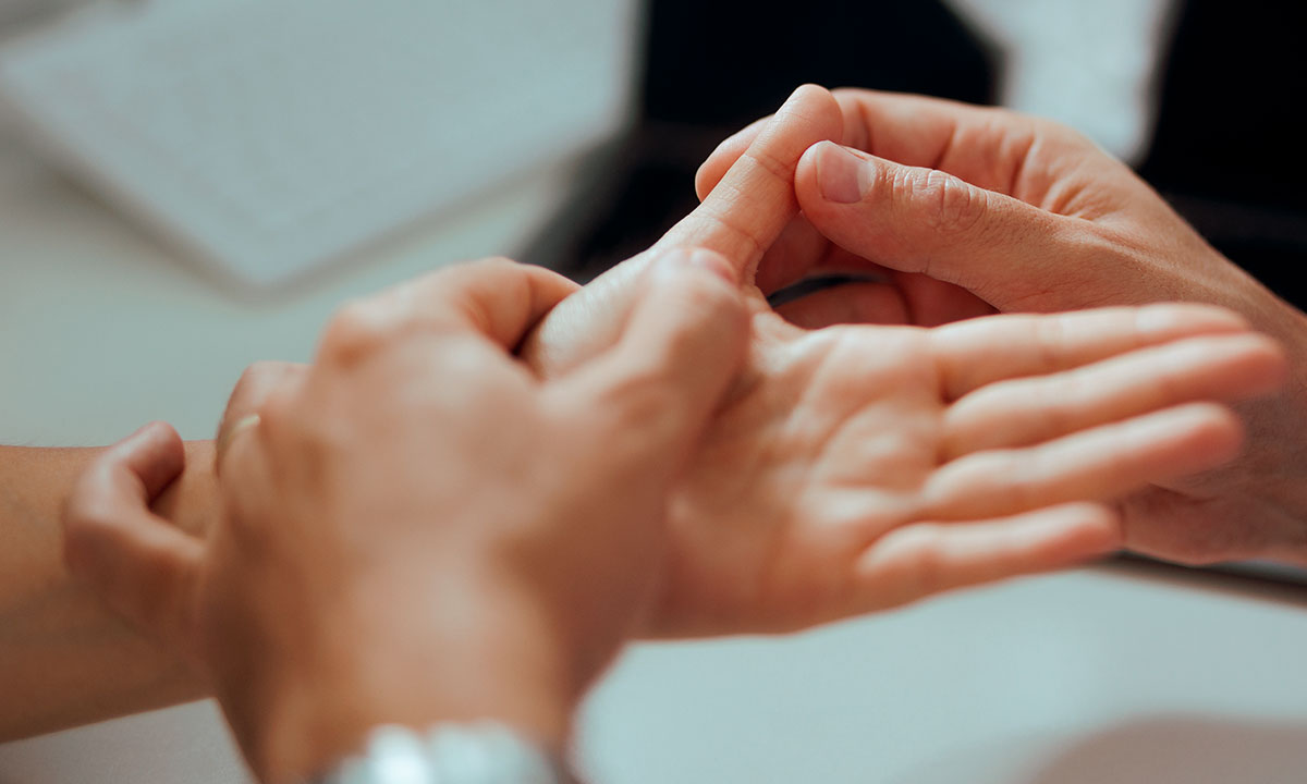 Læge undersøger patient med slidgigt i tommelfingeren.