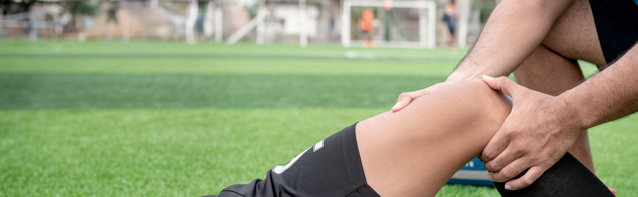 Fysioterapeut undersøger knæet på en fodboldspiller. som ligger på banen.