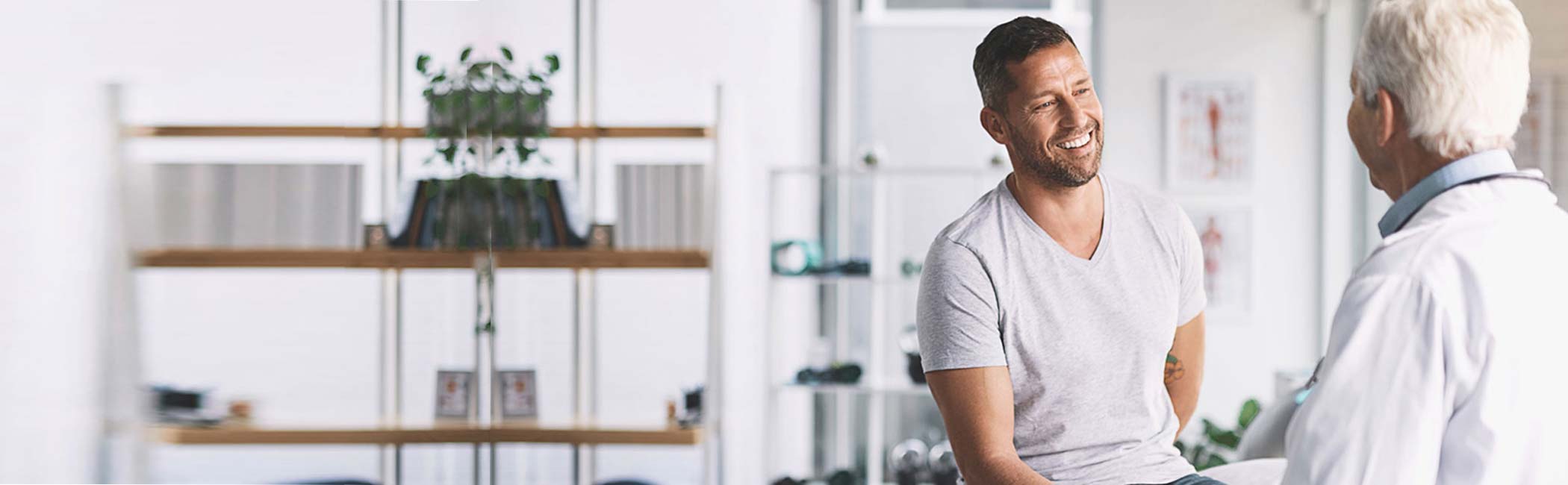 Læge taler med en glad mand i et konsultationsrum.