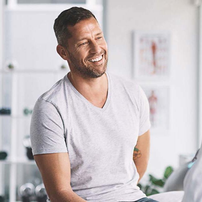 Læge taler med en glad mand i et konsultationsrum.