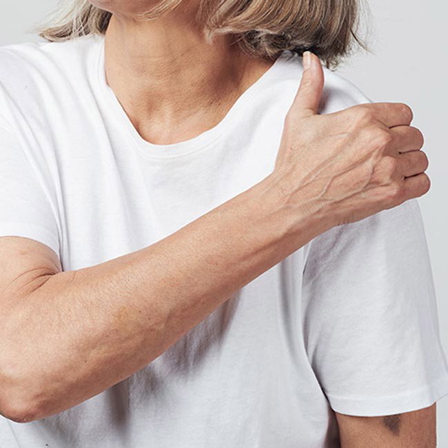 En kvinder tager sig til skulderen grundet skuldersmerter.