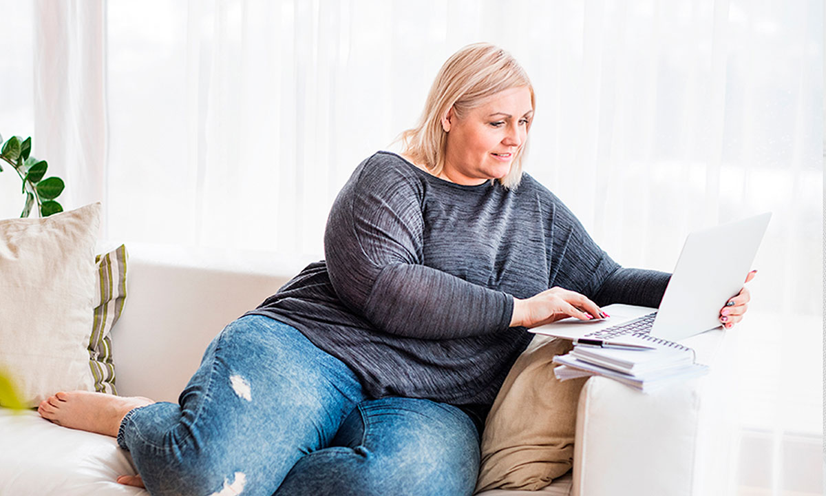 Kvinde sidder i en sofa med sin computer og læser om sine patientrettigheder.