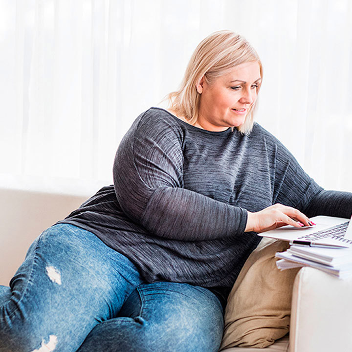 Kvinde sidder i en sofa med sin computer og læser om sine patientrettigheder.