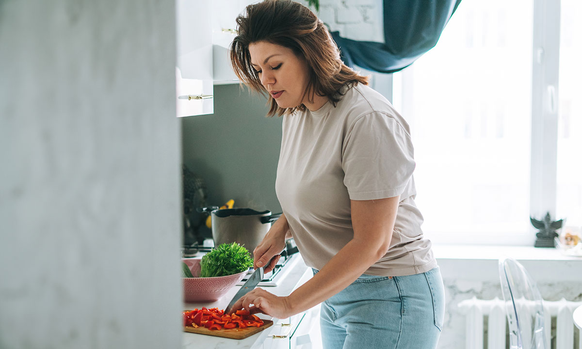 Kvinde står og forbereder mad i køkken efter råd fra en diætist.
