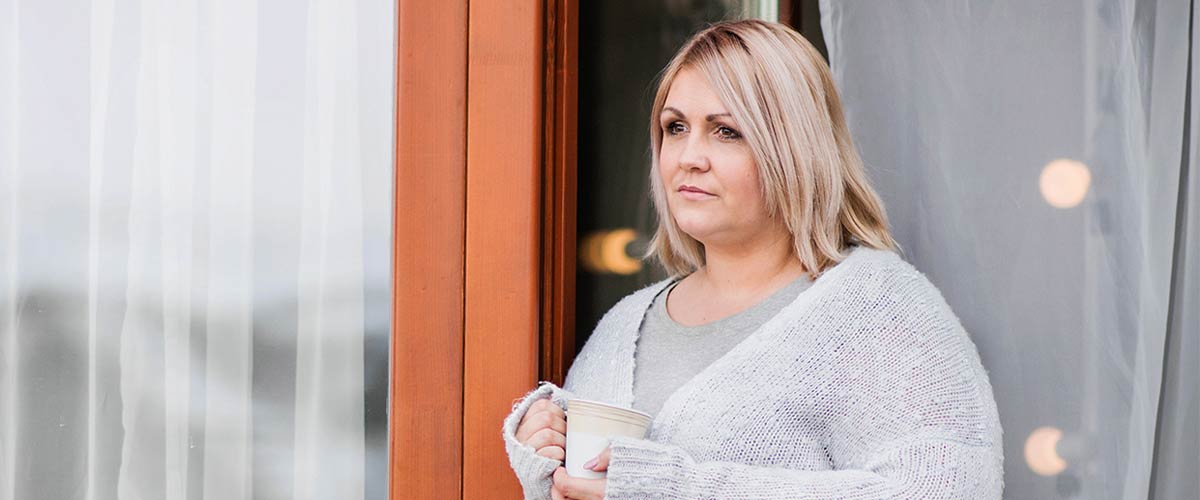 Overvægtig kvinde står i havedør og kigger ud.