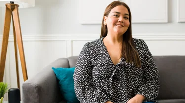 En kvinde sidder og smiler i en sofa.