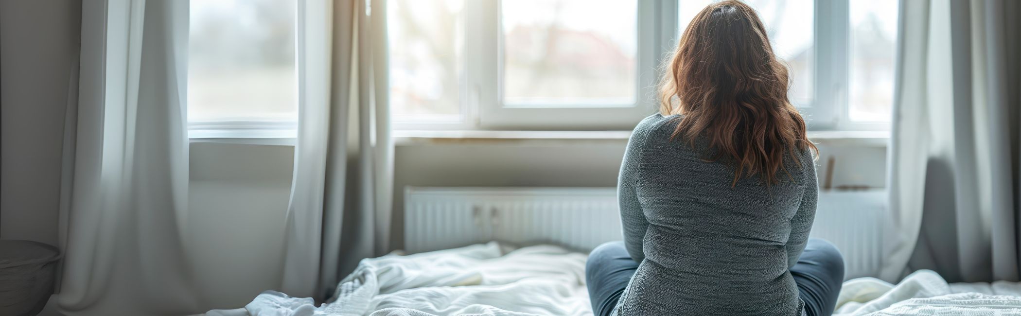 Kvinde sidder i en seng og kigger ud af vinduet.