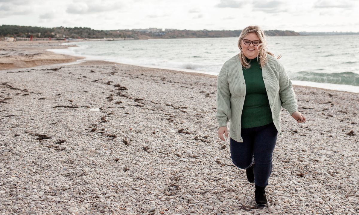 Overvægtig kvinde går på strand.