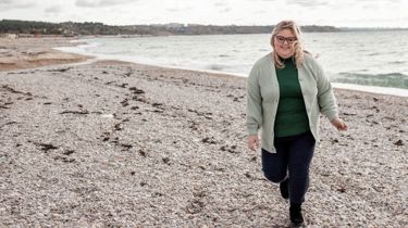 Overvægtig kvinde går på strand.